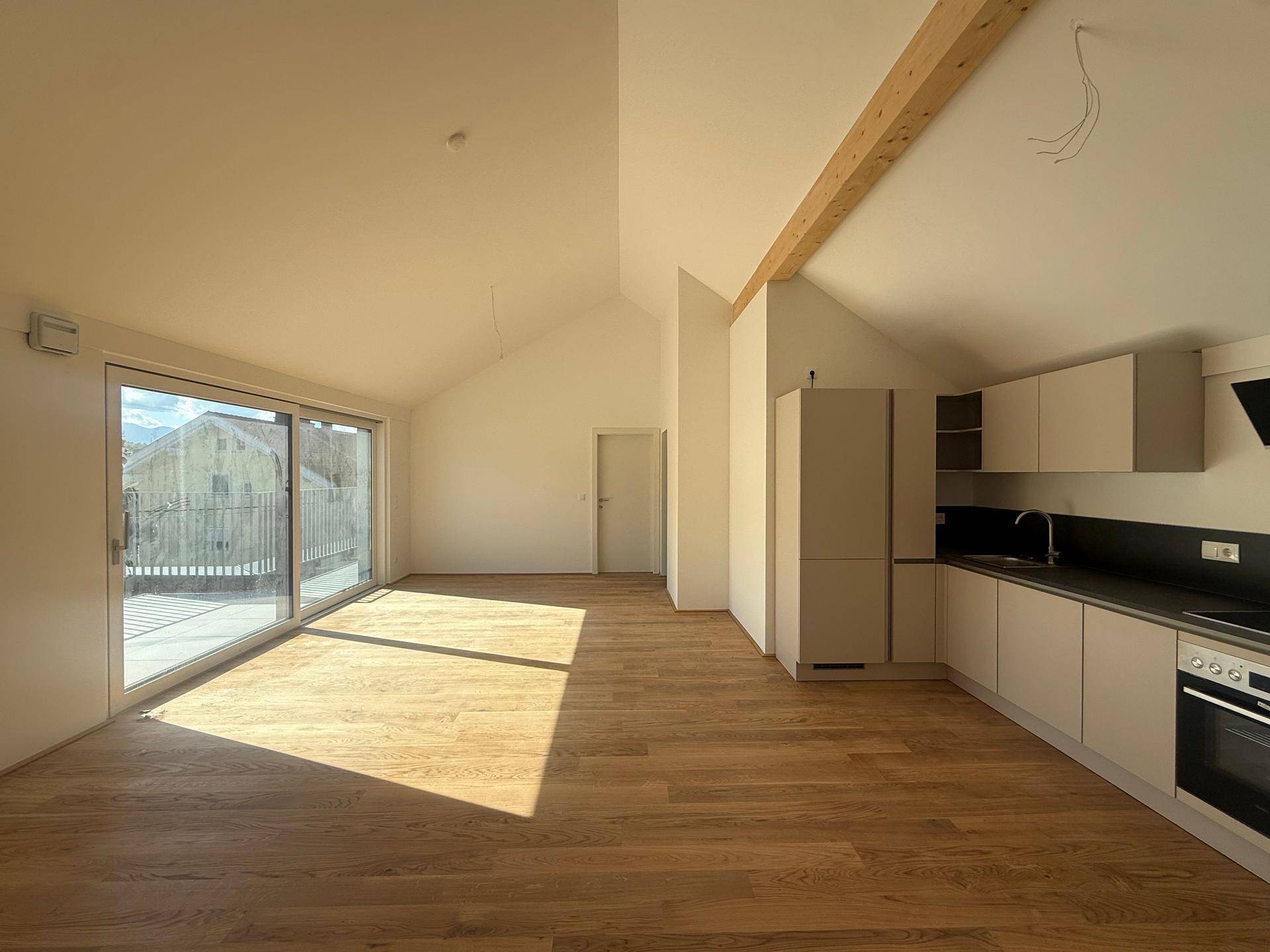 Heller, offener Wohn- und Essbereich mit integrierter Küche, Holzbalken und Zugang zur Terrasse.