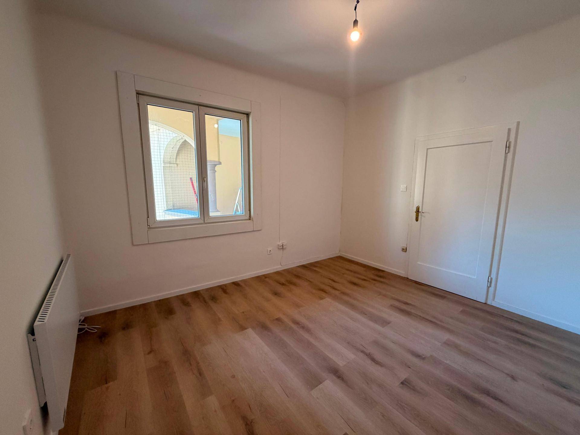 Leeres Zimmer mit Laminatboden, Heizkörper und Blick auf einen charmanten Innenhof.