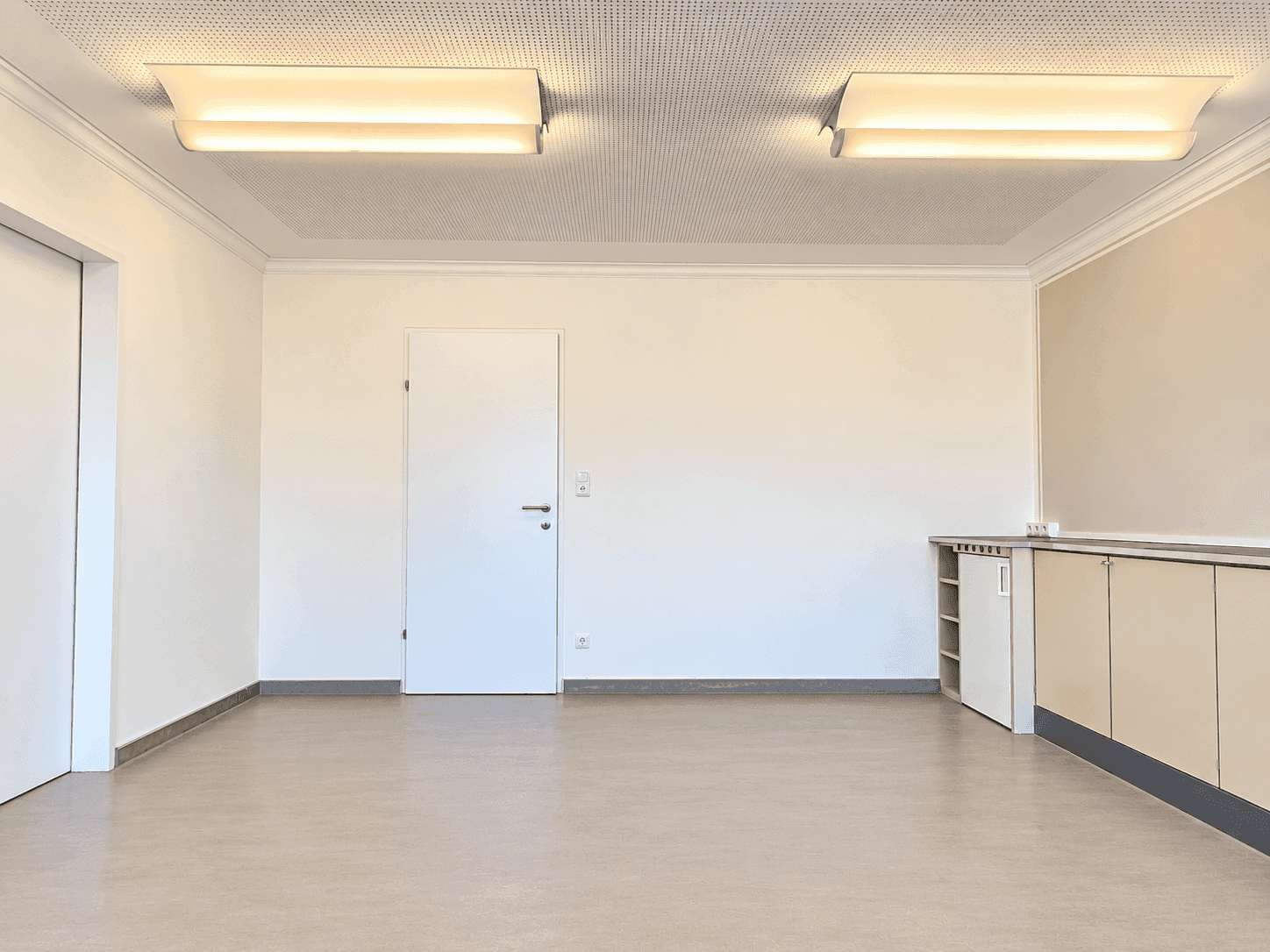 Leerer Mehrzweckraum mit weißer Tür, Einbauschrank und hellem Boden.