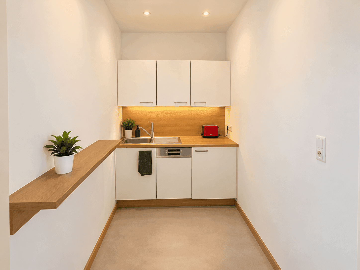 Kleine, moderne Küchenzeile mit weißen Schränken, Holztheke und integriertem Geschirrspüler.
