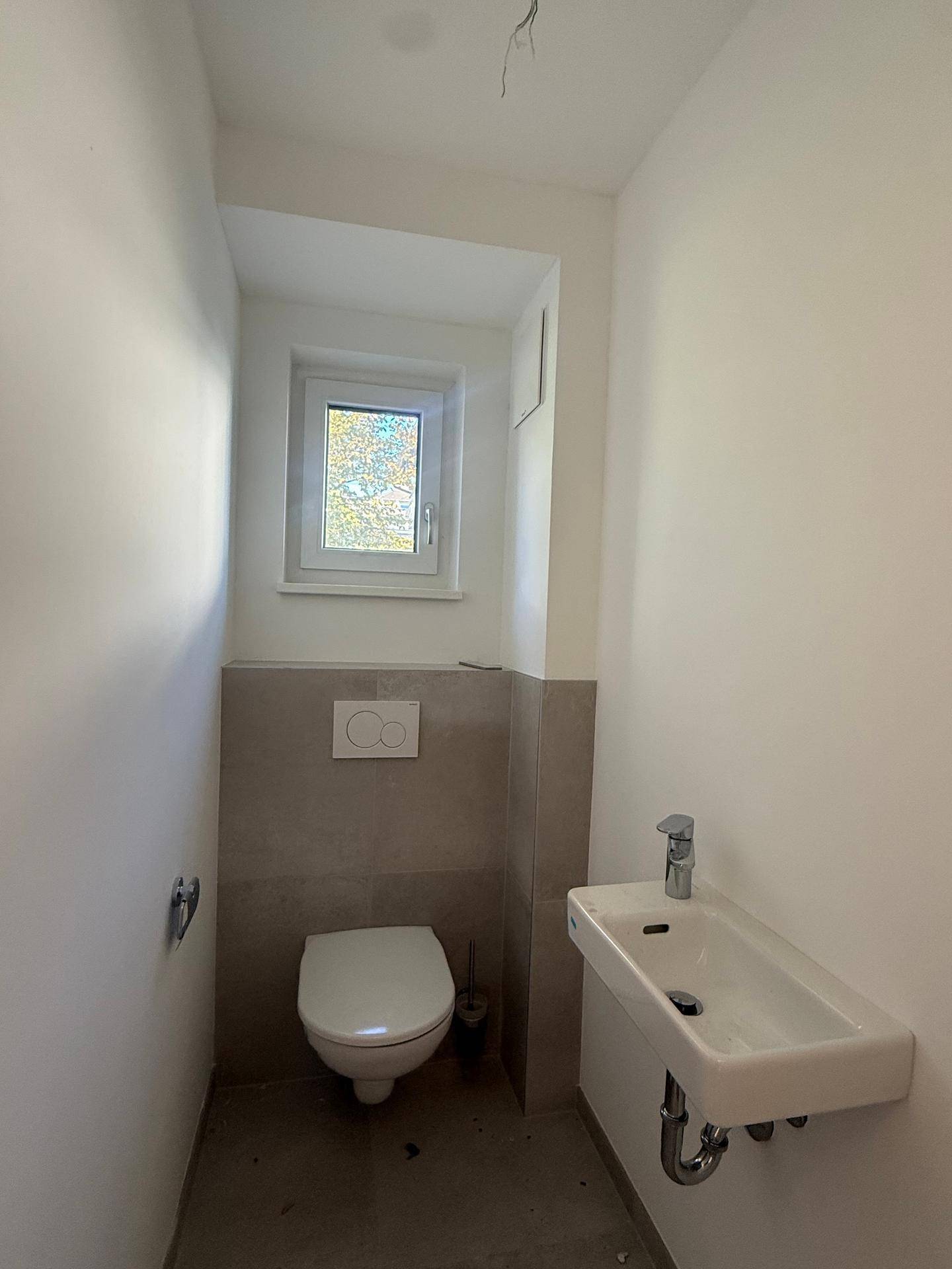 Separates Gäste-WC mit wandhängender Toilette, kleinem Waschbecken und Fenster.