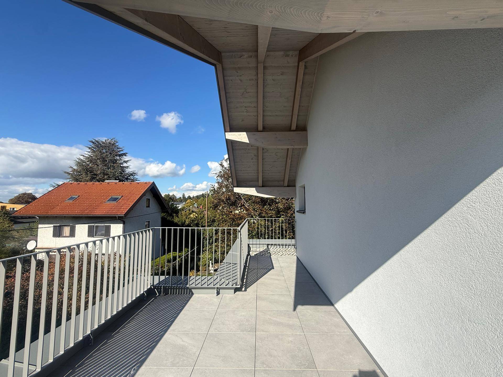 Geräumige Terrasse mit Fliesenboden und Blick auf die umliegende Wohngegend und Bäume.