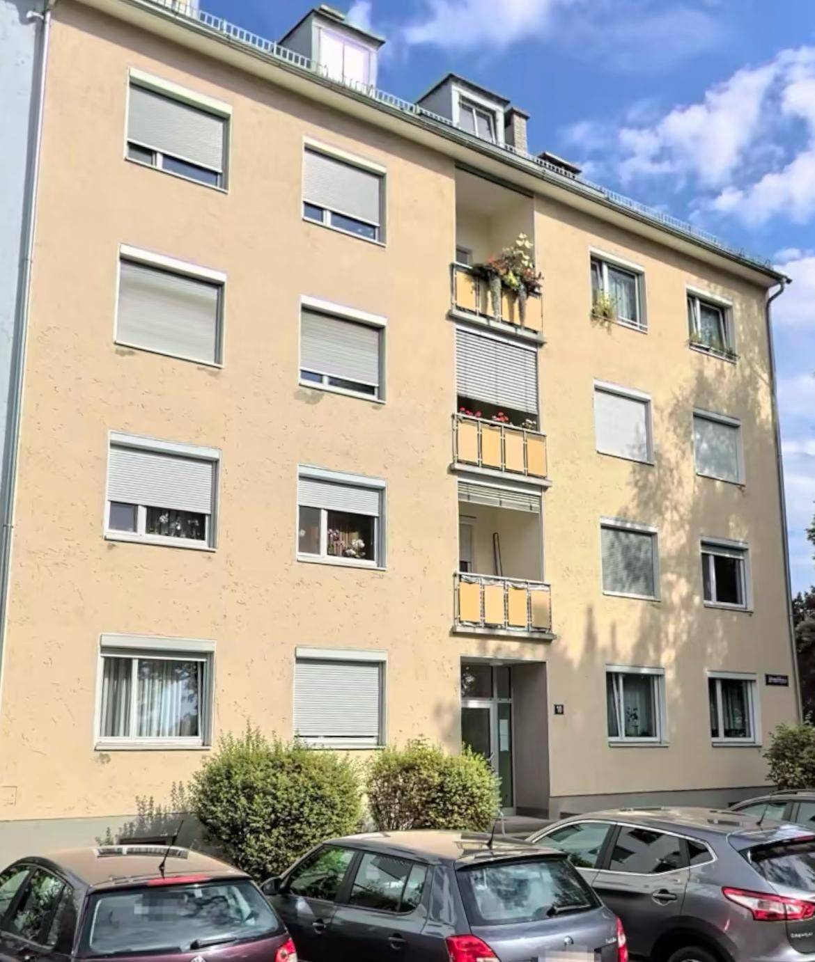 Mehrfamilienhaus mit gelber Fassade, Balkonen und vielen Fenstern.