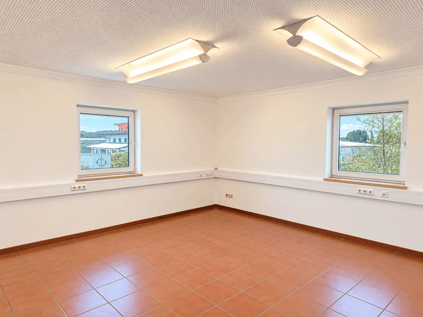 Geräumiger Büroraum mit zwei Fenstern, Fliesenboden und abgehängter Decke.