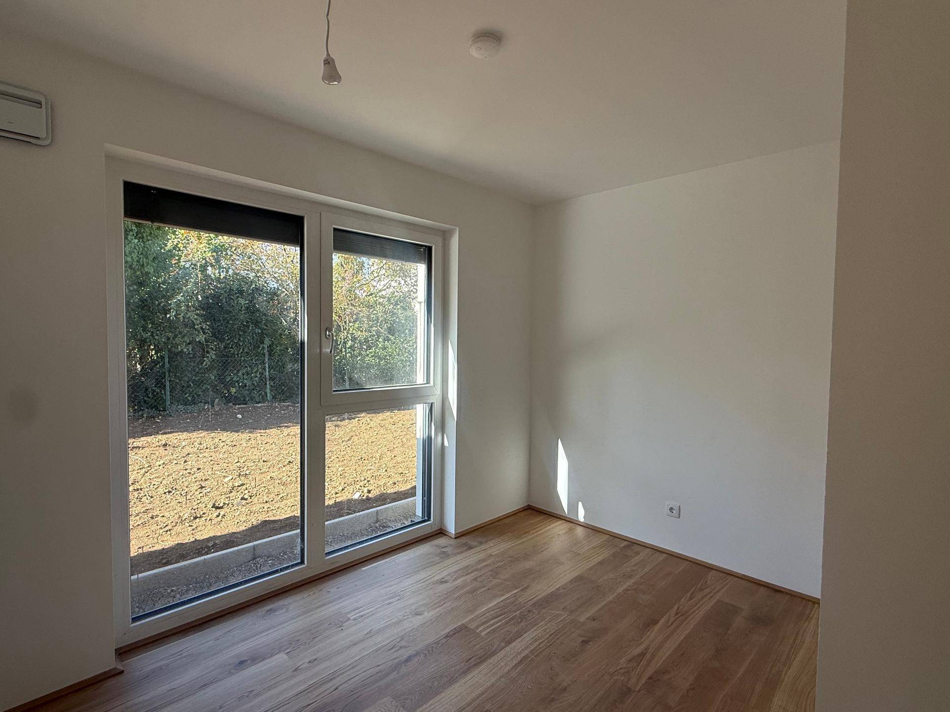 Helles Schlafzimmer mit großen Fenstern und Blick auf den Gartenbereich.