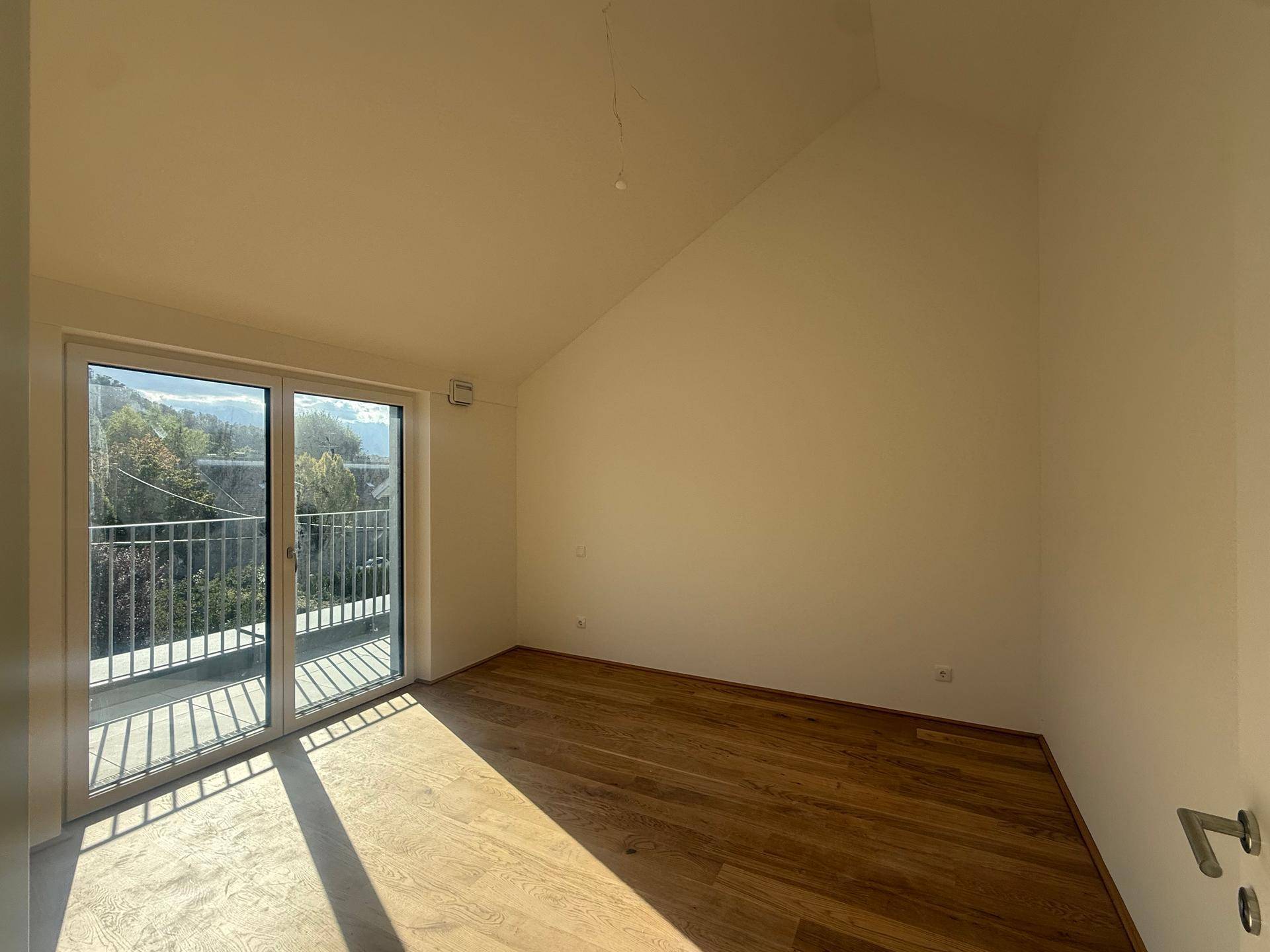 Lichtdurchflutetes Zimmer mit Holzboden, Dachschräge und direktem Zugang zu einem Außenbereich.