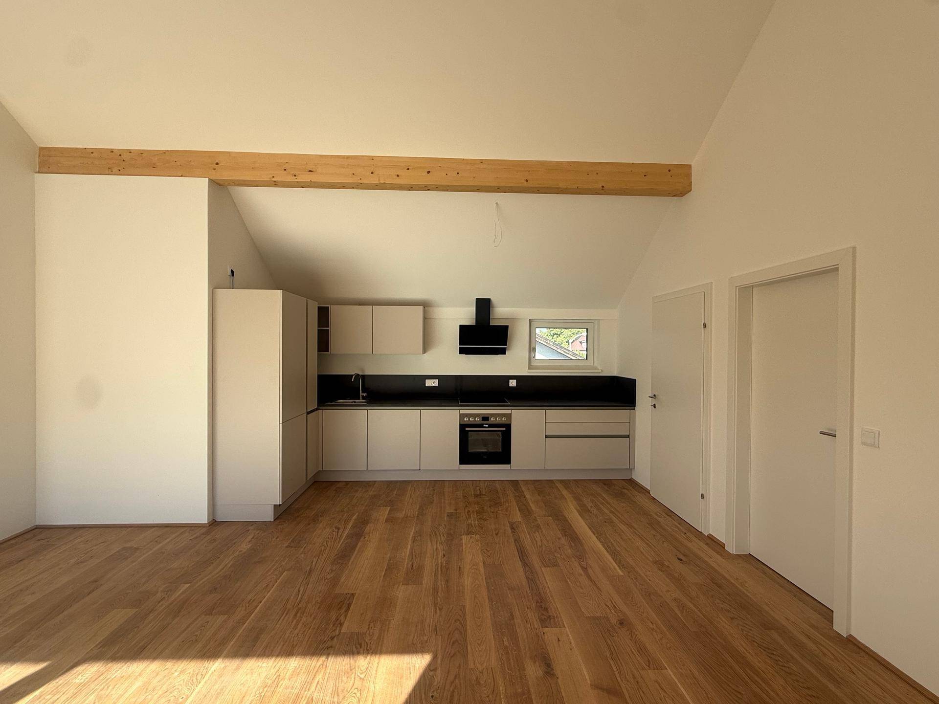 Moderne Einbauküche im offenen Wohnbereich mit Dachschrägen, Holzbalken und hochwertigen Geräten.