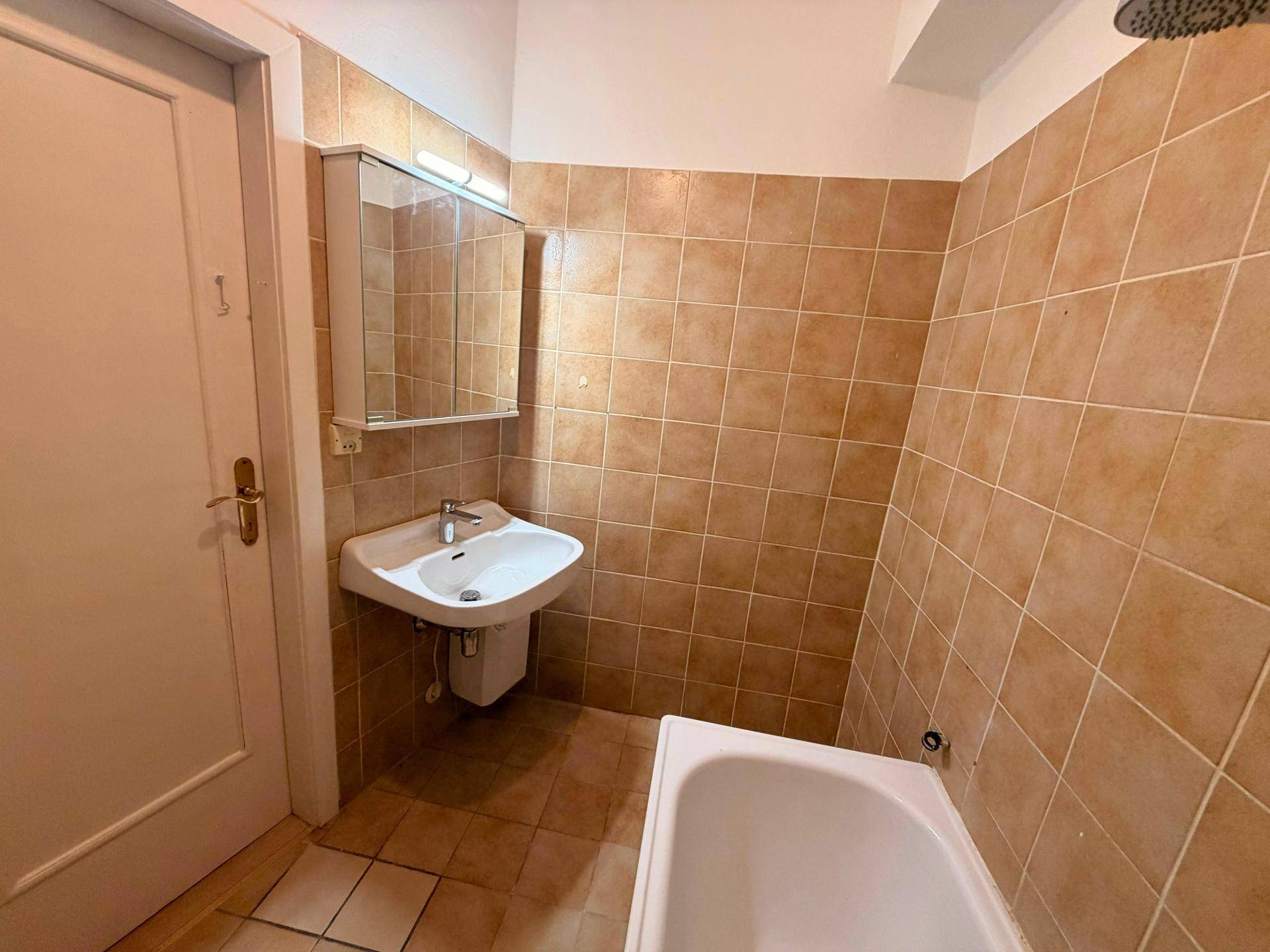 Badezimmer mit braunen Fliesen, Badewanne und Waschbecken mit Spiegelschrank, funktional und gepflegt.