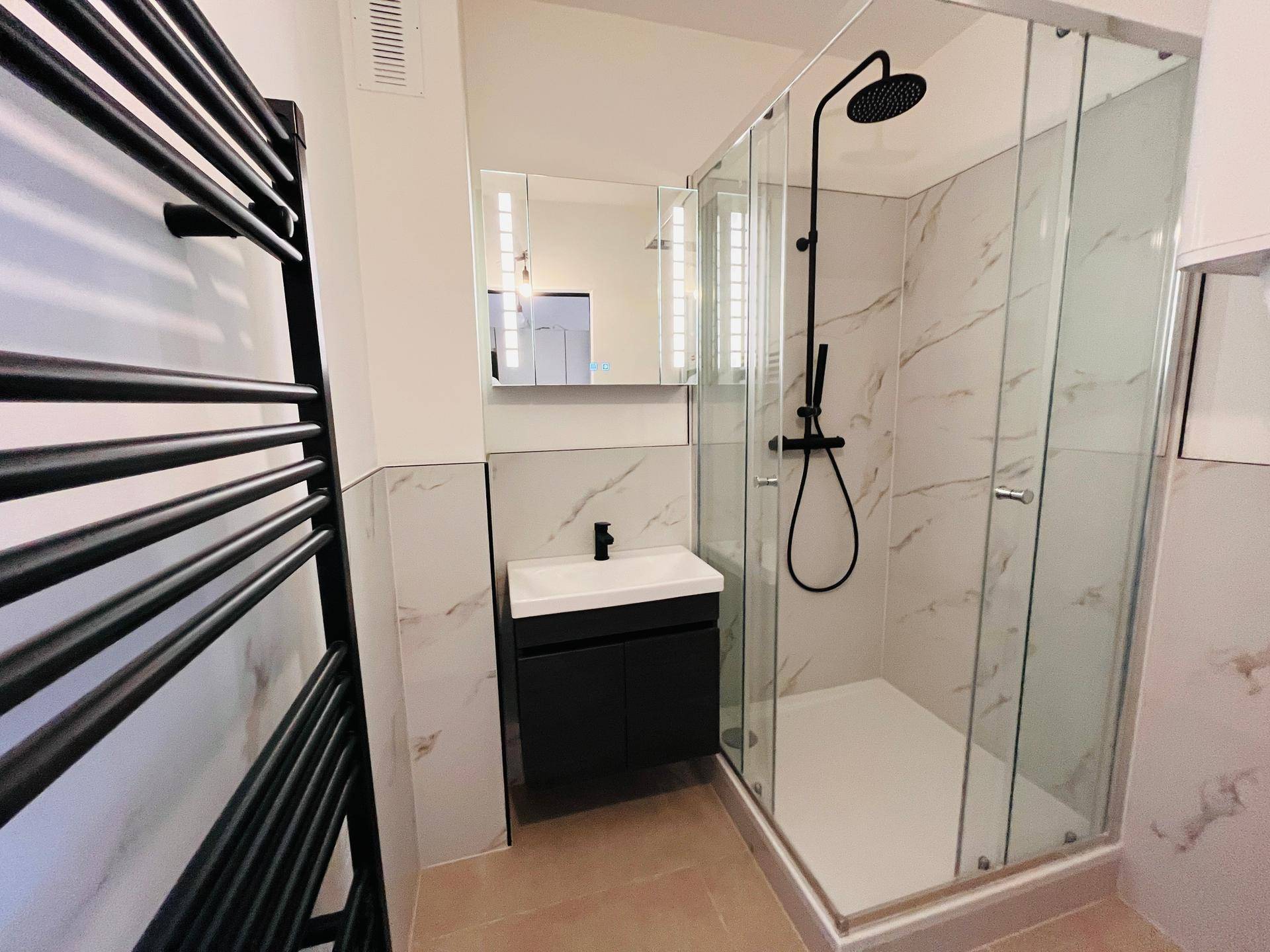 Modernes Badezimmer mit Duschkabine, Einzelwaschbecken, Spiegelschrank und beheiztem Handtuchhalter.