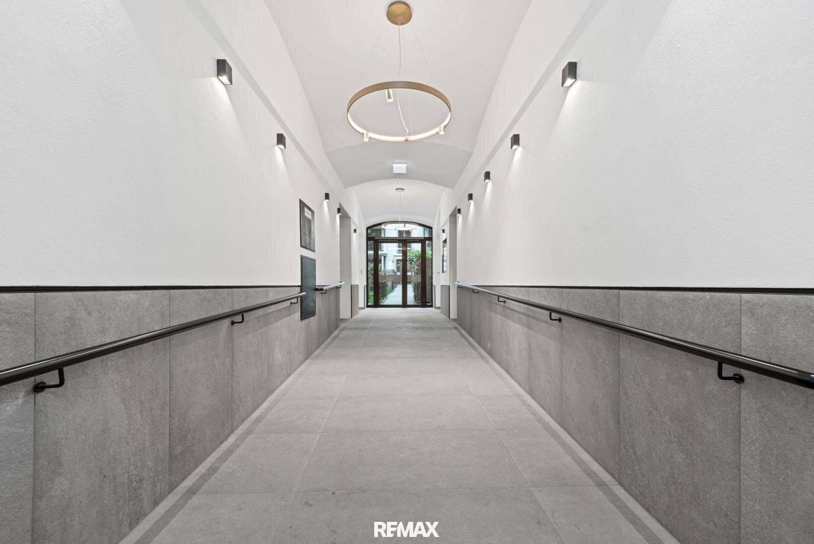 Langer, heller Flur mit gewölbter Decke, modernen Leuchten und Handläufen an den Wänden.