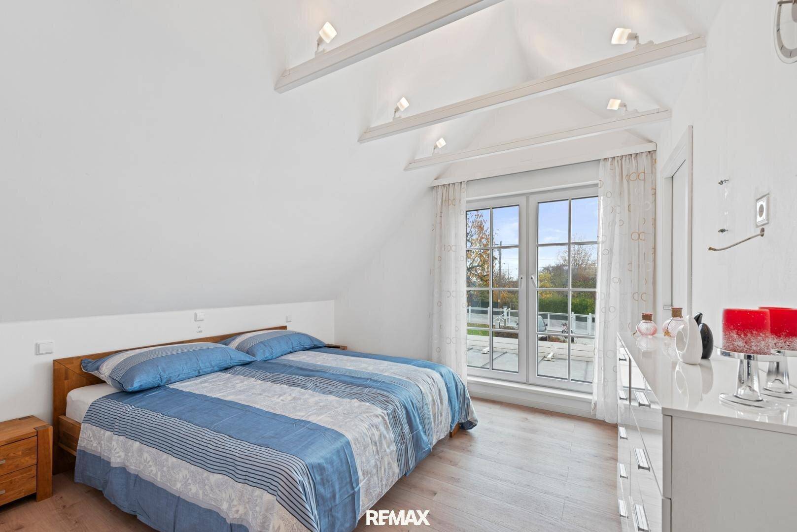 Schlafzimmer im Dachgeschoss mit Holzbett, Kommode und Blick nach draußen.