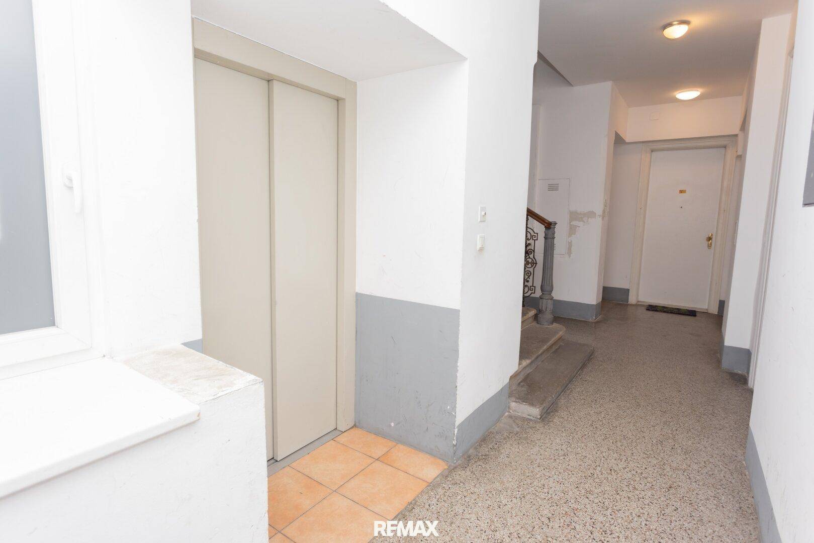 Heller Flur im Treppenhaus mit Aufzug und Terrazzoboden, der zu den Wohnungen führt.