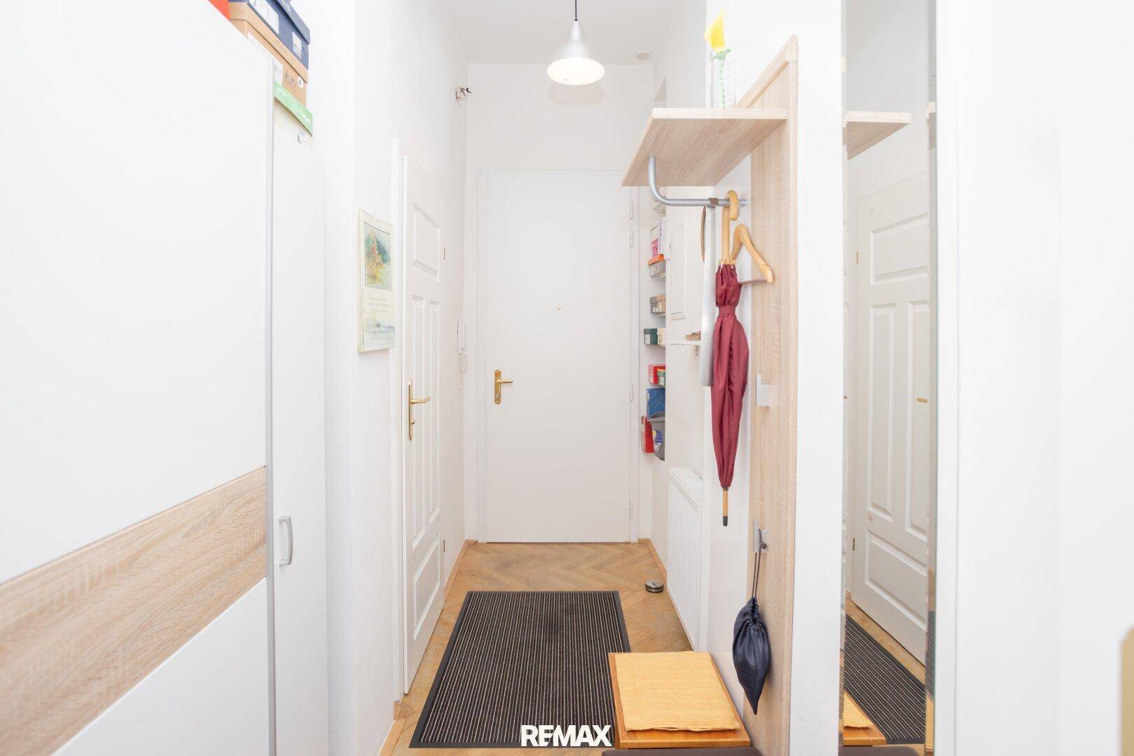 Heller Eingangsbereich der Wohnung mit Garderobe, Spiegel und Parkettboden.