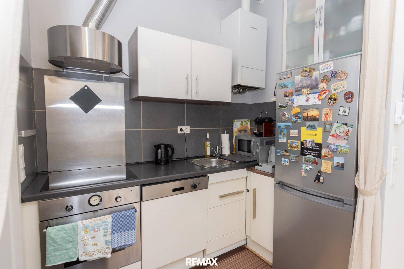 Kleine Einbauküche mit modernen Geräten, Edelstahl-Dunstabzugshaube und Kühlschrank.