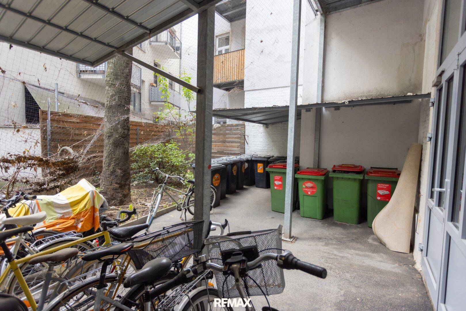 Fahrradabstellplatz im Freien mit Mülltonnen und Überdachung im Hinterhof.