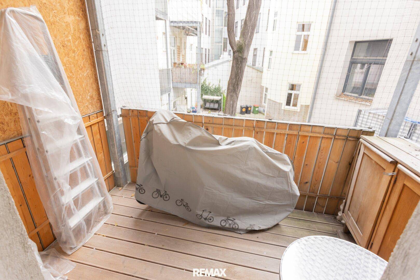 Kleiner Balkon mit Holzfußboden, Sichtschutz und Blick auf den Innenhof.