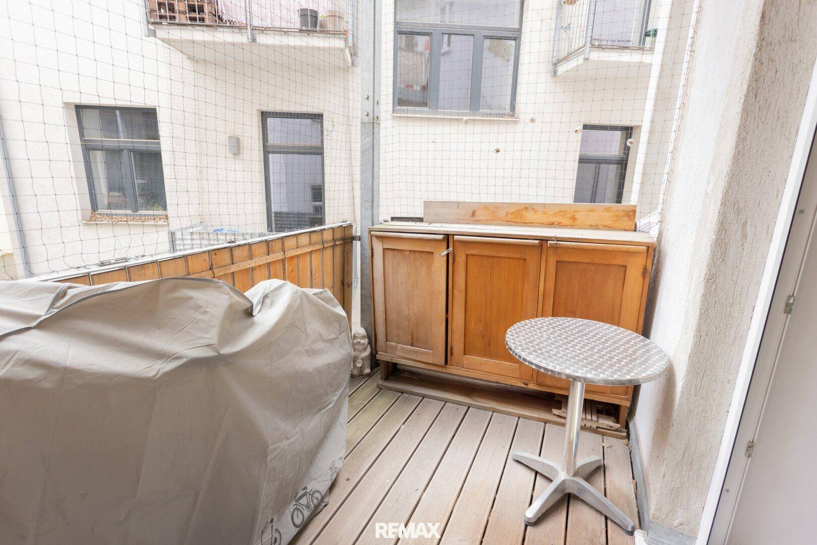 Balkon mit Holzboden, kleinem Tisch und Schrank, der zum Innenhof ausgerichtet ist.