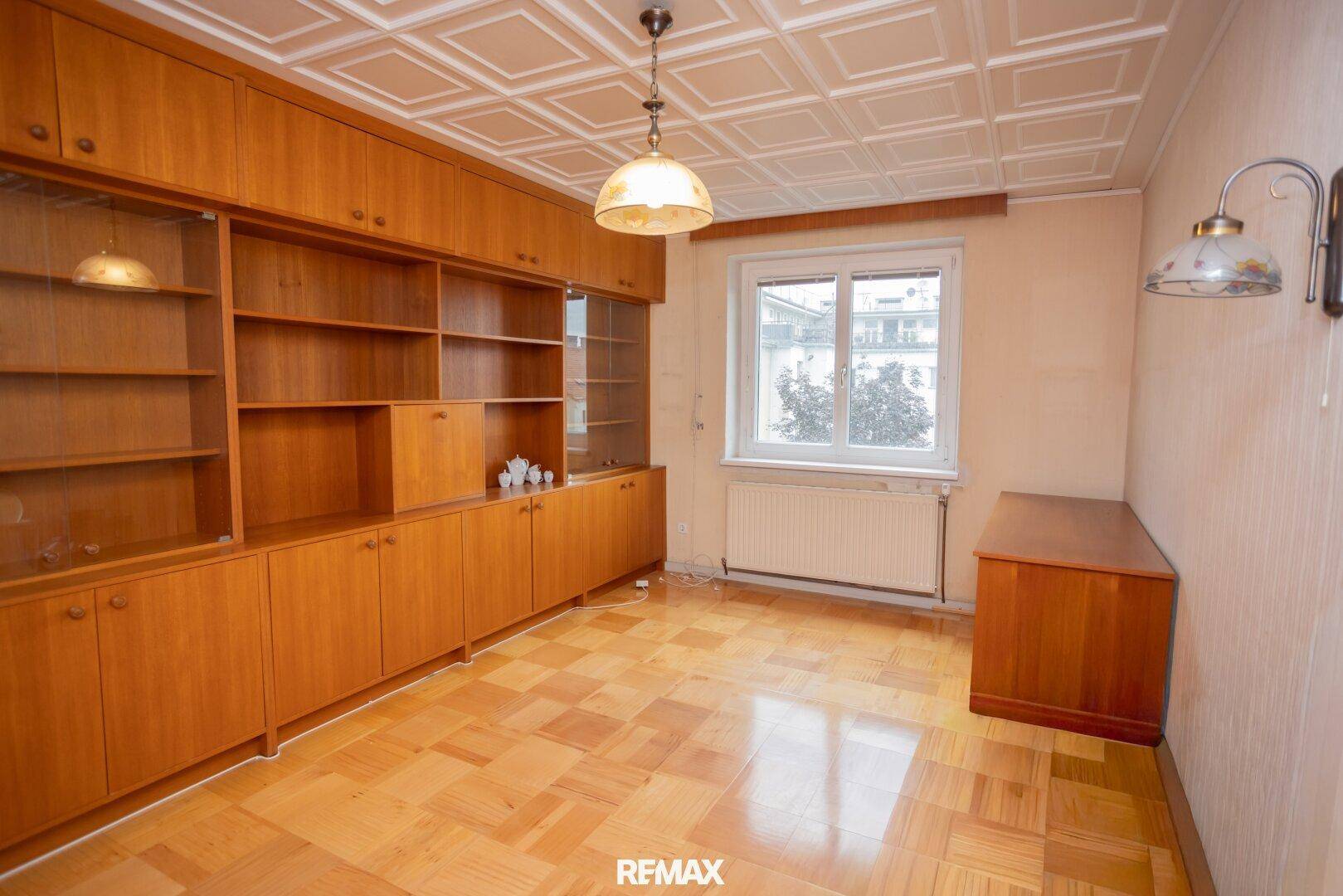 Wohnzimmer mit Holzparkett, Einbauschränken und einer dekorativen Deckenverkleidung, die Charakter verleiht.
