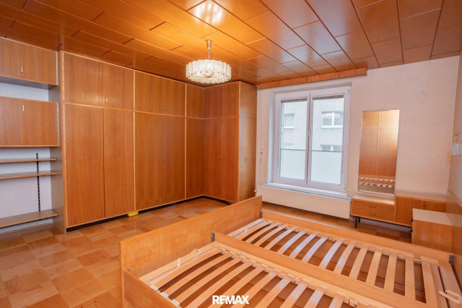 Schlafzimmer mit umfangreichen Holzschränken, Parkettboden und einem großen Fenster für viel Tageslicht.