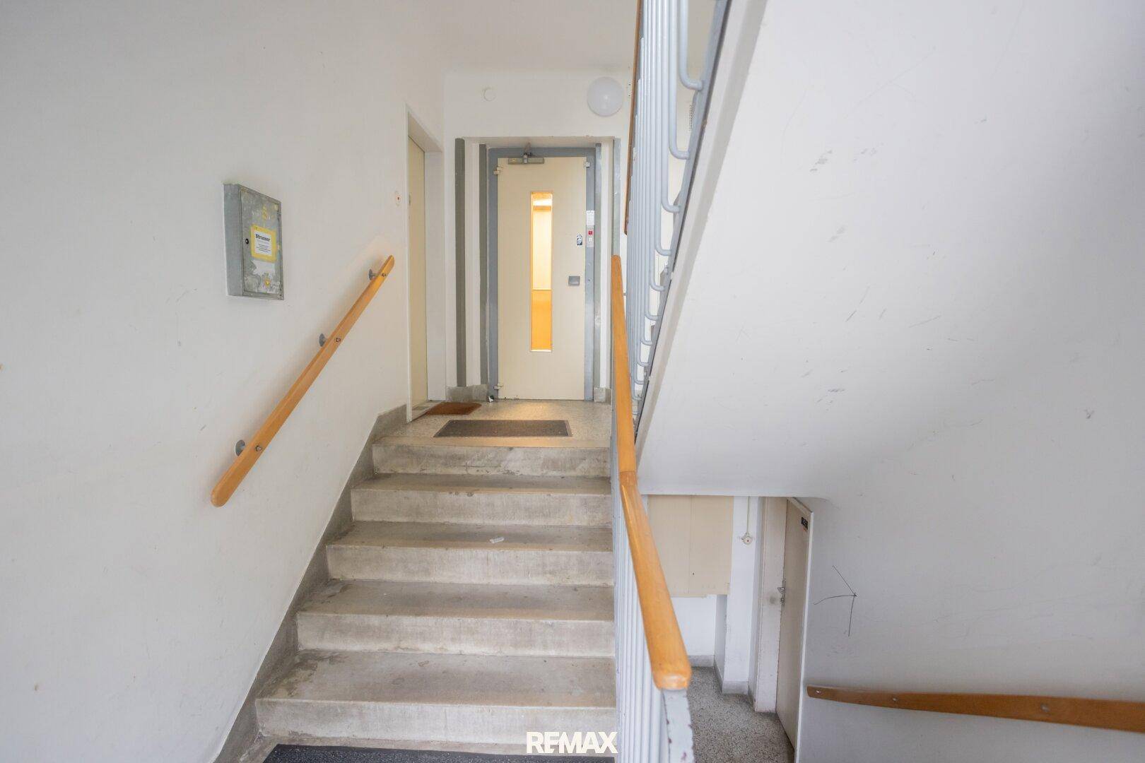 Treppenhaus mit Betontreppen und Holzgeländer in einem Mehrfamilienhaus, das zu den oberen Etagen führt.