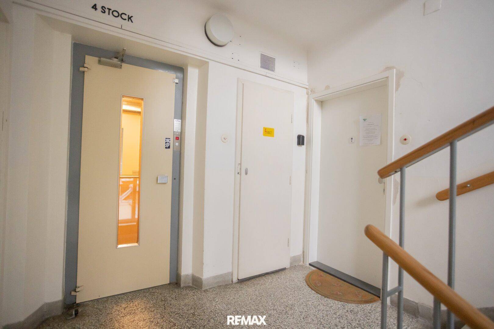 Treppenabsatz im vierten Stock mit Wohnungstüren und Terrazzoboden, der einen Zugang zum Aufzug bietet.