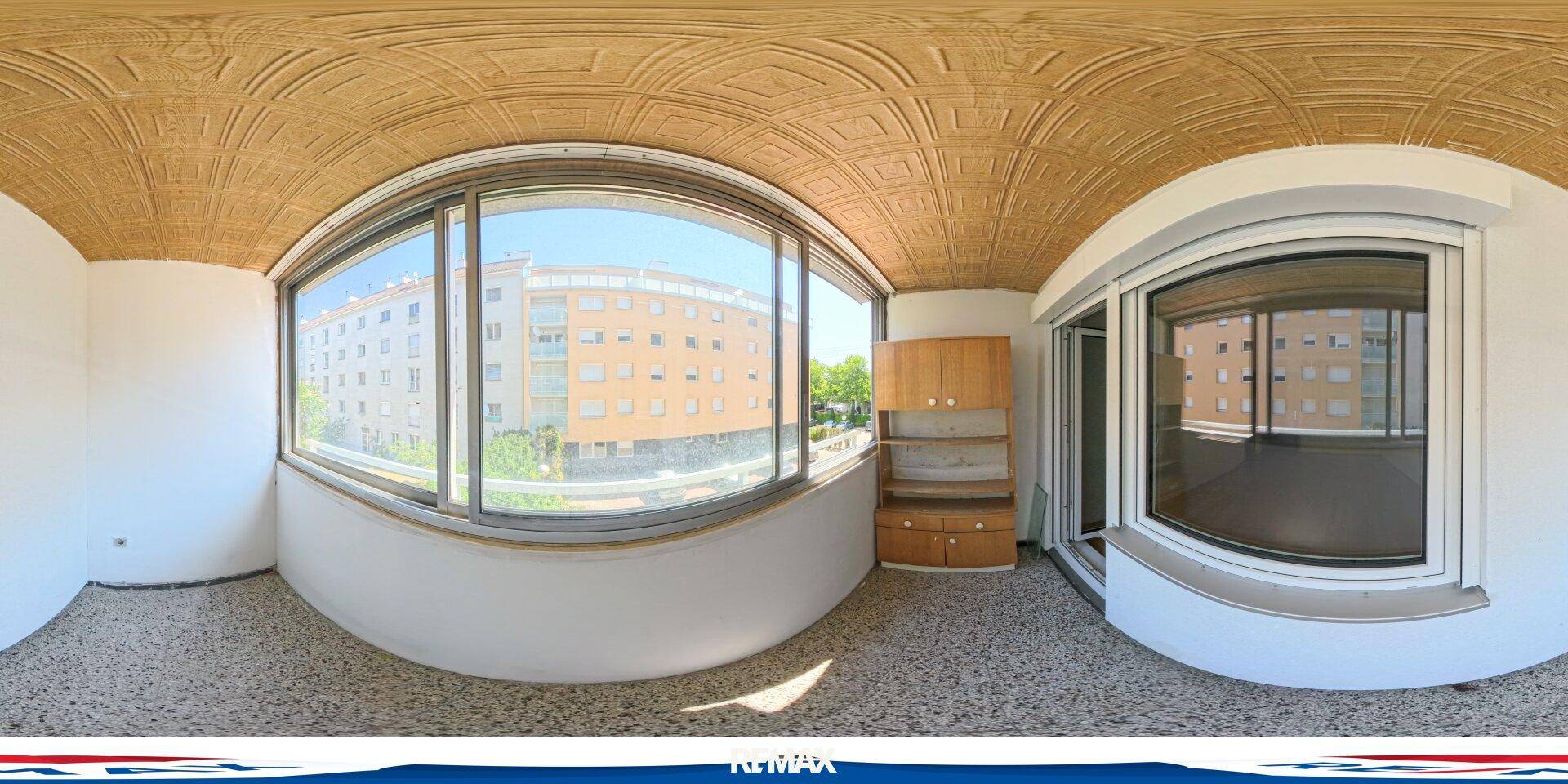 Verglaste Loggia mit großen Fenstern, Blick auf umliegende Gebäude und einem kleinen Schrank.