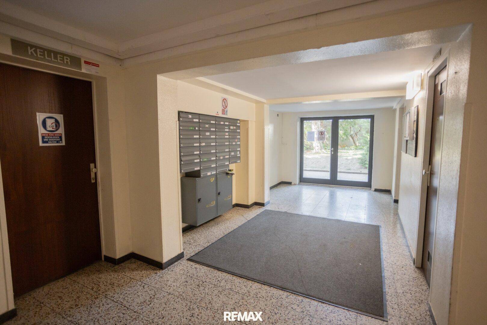 Eingangsbereich eines Mehrfamilienhauses mit Briefkästen, Fliesenboden und Zugang zum Keller.