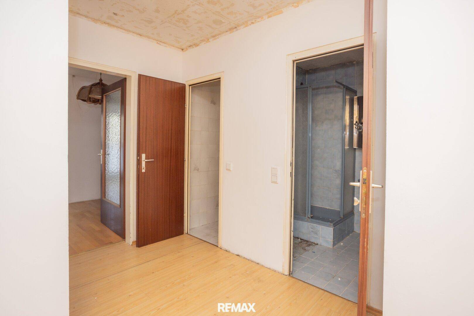 Flur mit Holzboden und Zugang zu verschiedenen Räumen, darunter ein Badezimmer mit Dusche.