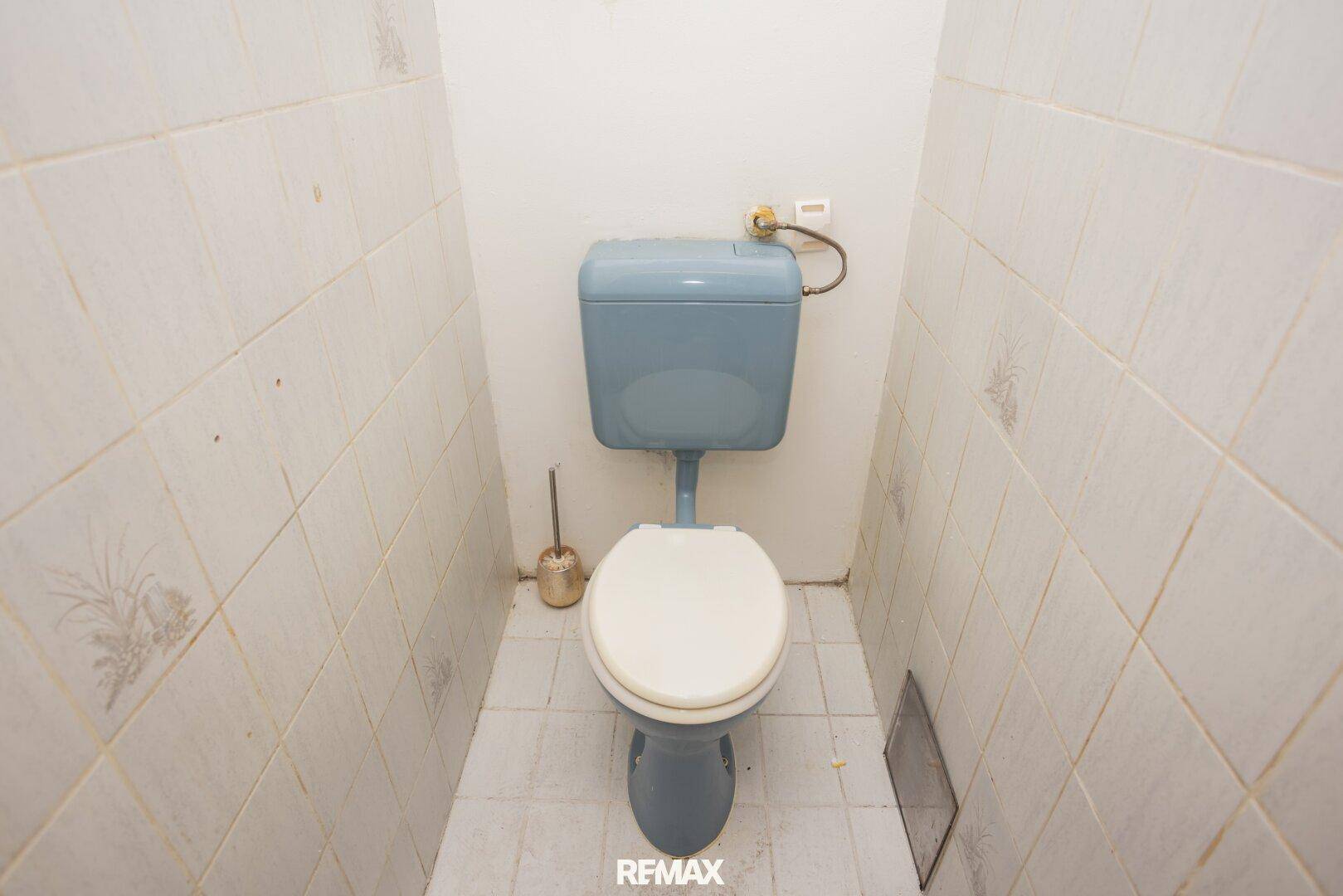 Separate Toilette mit blauer Keramik und weißen Wandfliesen, in originalem Zustand.