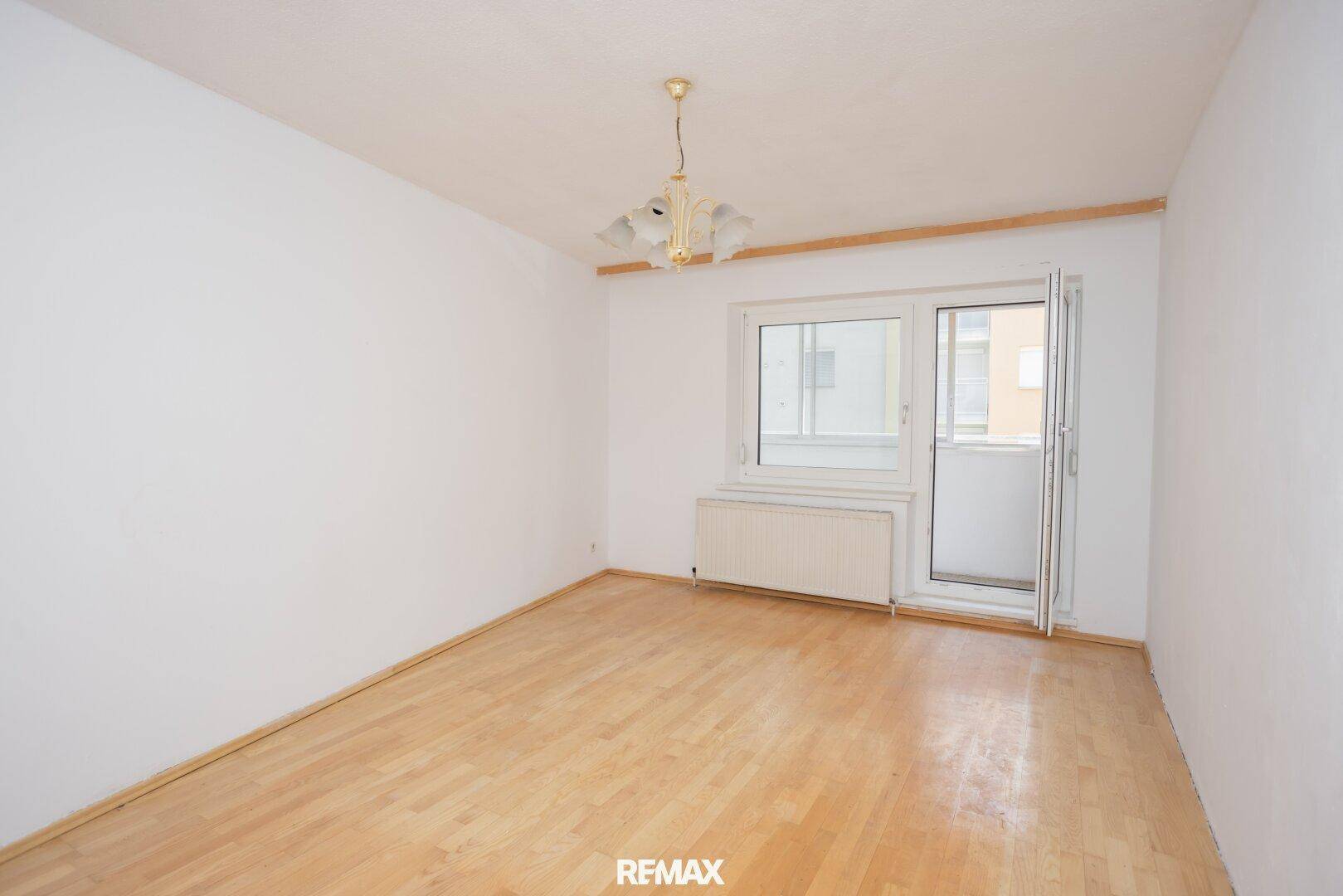Helles Wohnzimmer mit Holzboden und Zugang zum Balkon, unmöbliert und geräumig.