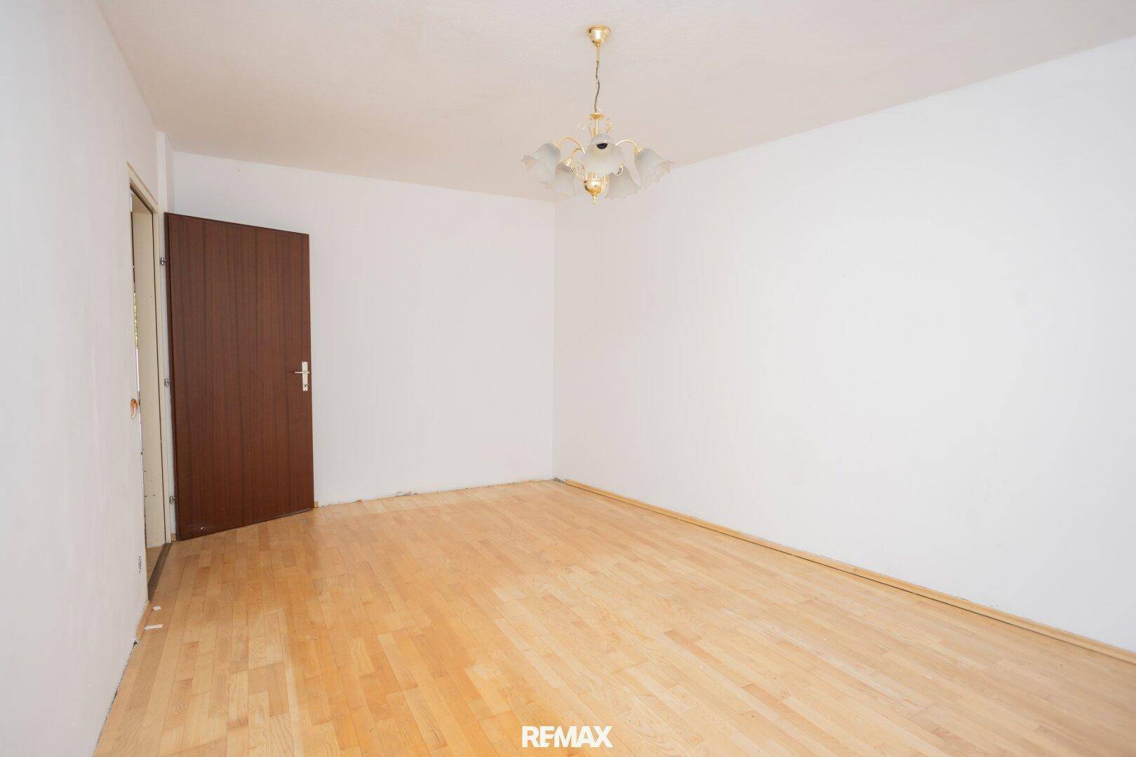 Geräumiges Wohnzimmer mit Holzboden und Holztür, unmöbliert und hell.