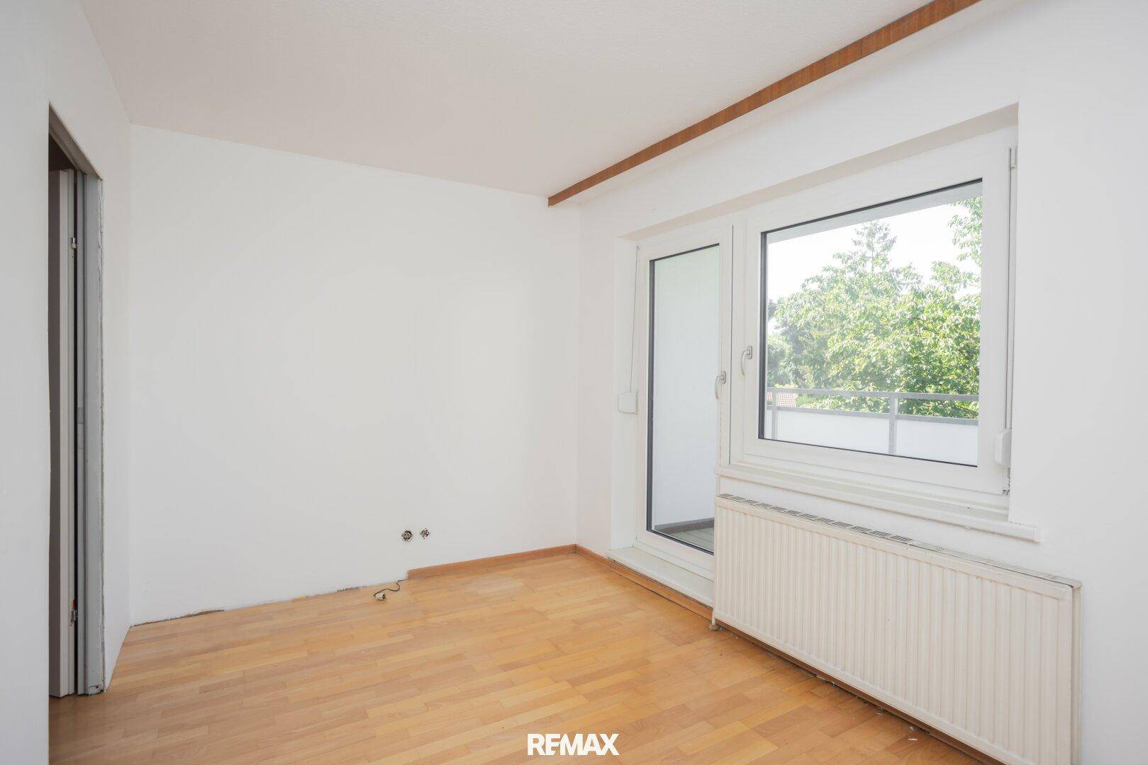 Schlafzimmer mit Holzboden und Fenster, das viel Tageslicht hereinlässt und Blick ins Grüne bietet.