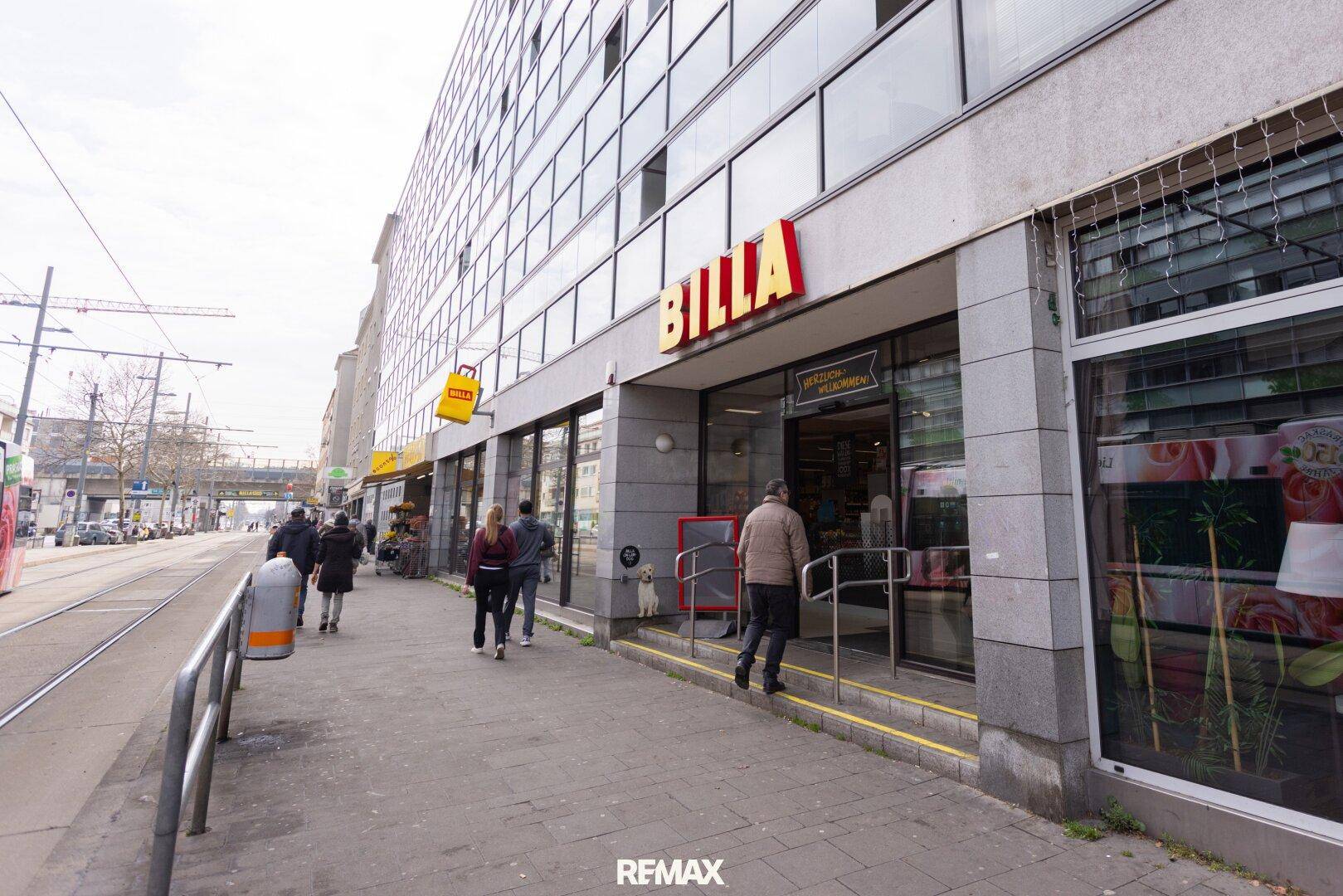 Eingang eines BILLA Supermarktes an einer belebten Straße mit Straßenbahnschienen.