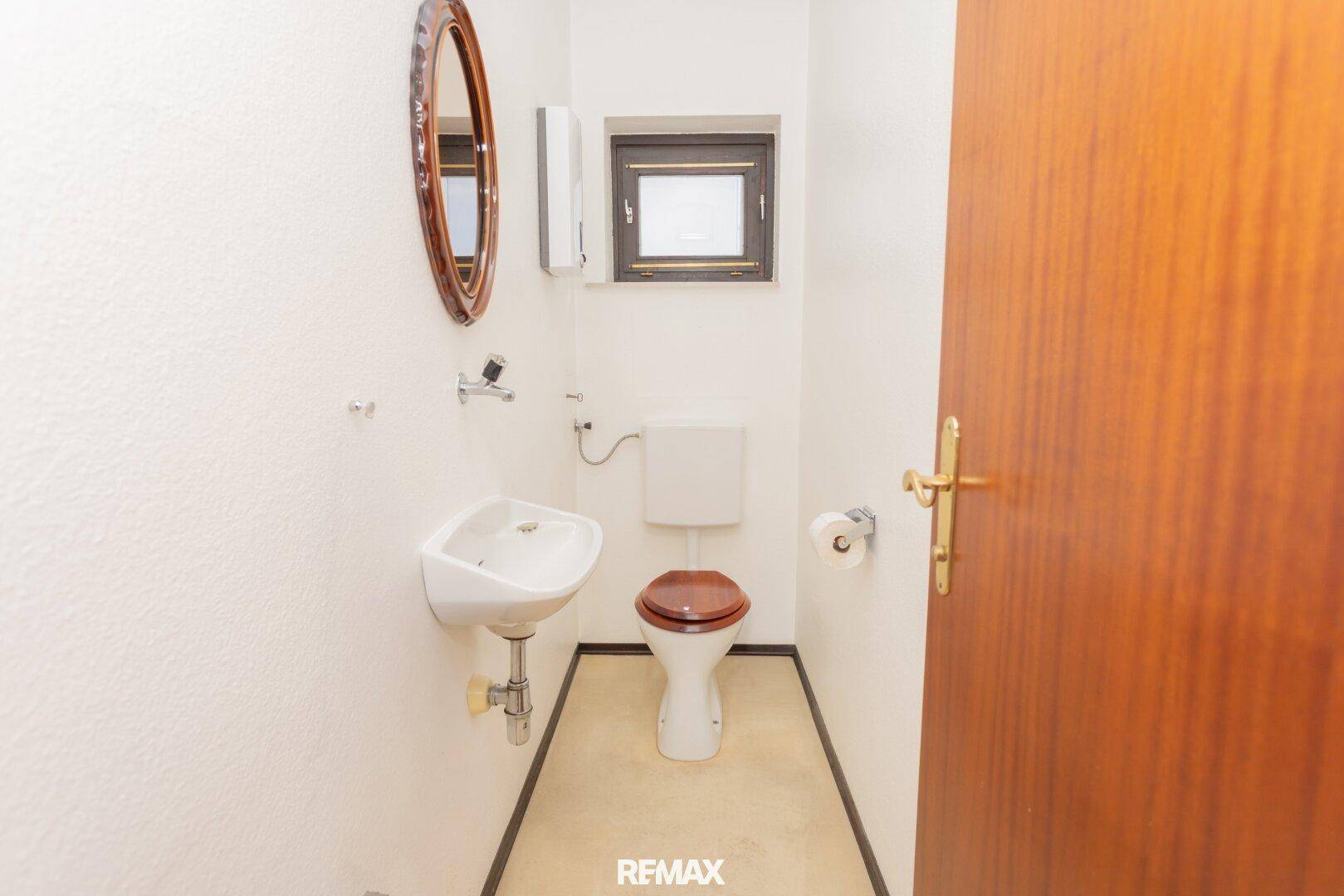 Separate Gästetoilette mit kleinem Waschbecken, WC und ovalem Spiegel.