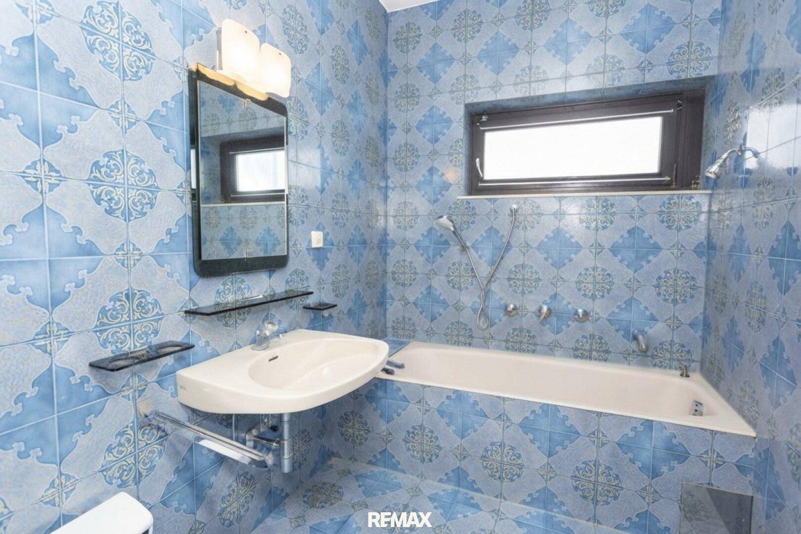 Badezimmer mit blauen gemusterten Fliesen, Badewanne und Waschbecken.