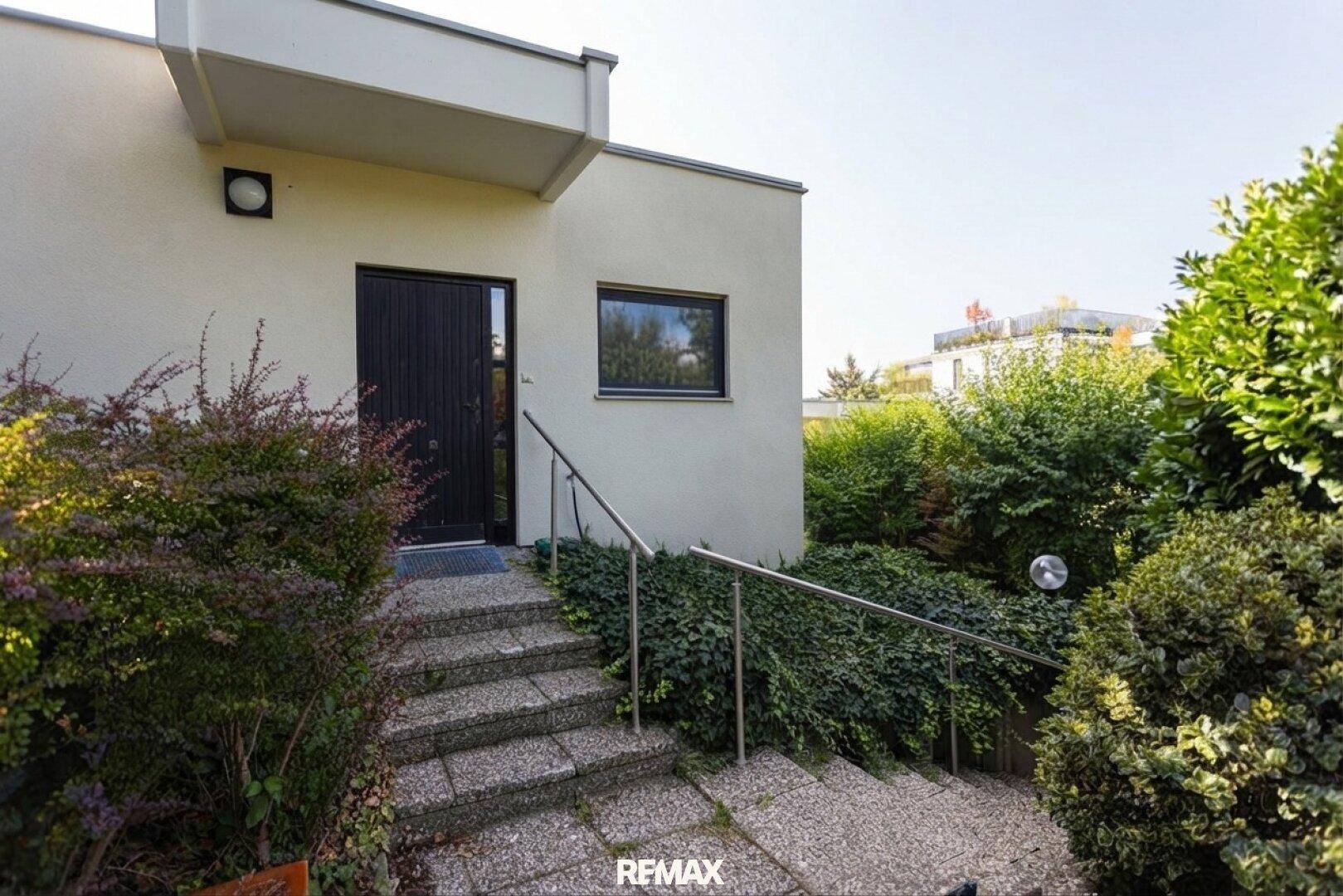 Eingangsbereich des Hauses mit Steintreppe, Metallgeländer und umgebenden Sträuchern.