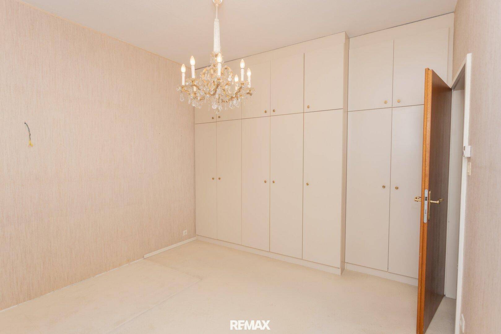 Schlafzimmer mit umfangreichen Einbauschränken und einem opulenten Kronleuchter.