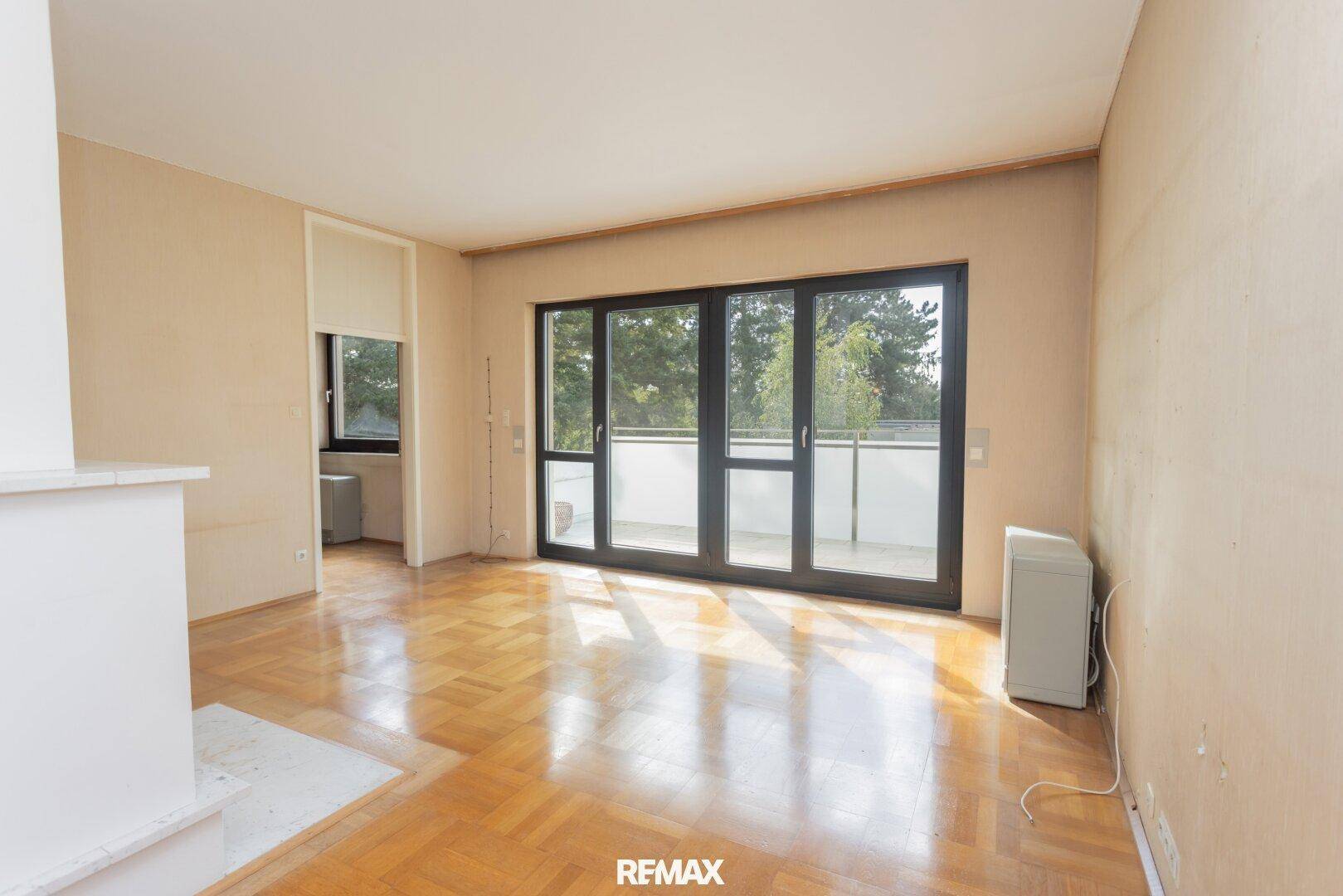Geräumiges Wohnzimmer mit Parkettboden und großen Schiebetüren zum Balkon.