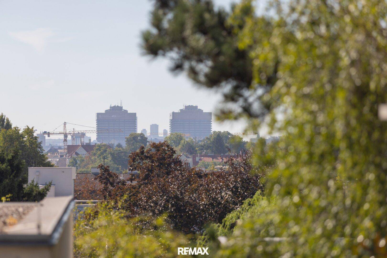 Panoramablick über die Stadt mit markanten Gebäuden und grünen Baumwipfeln im Vordergrund.