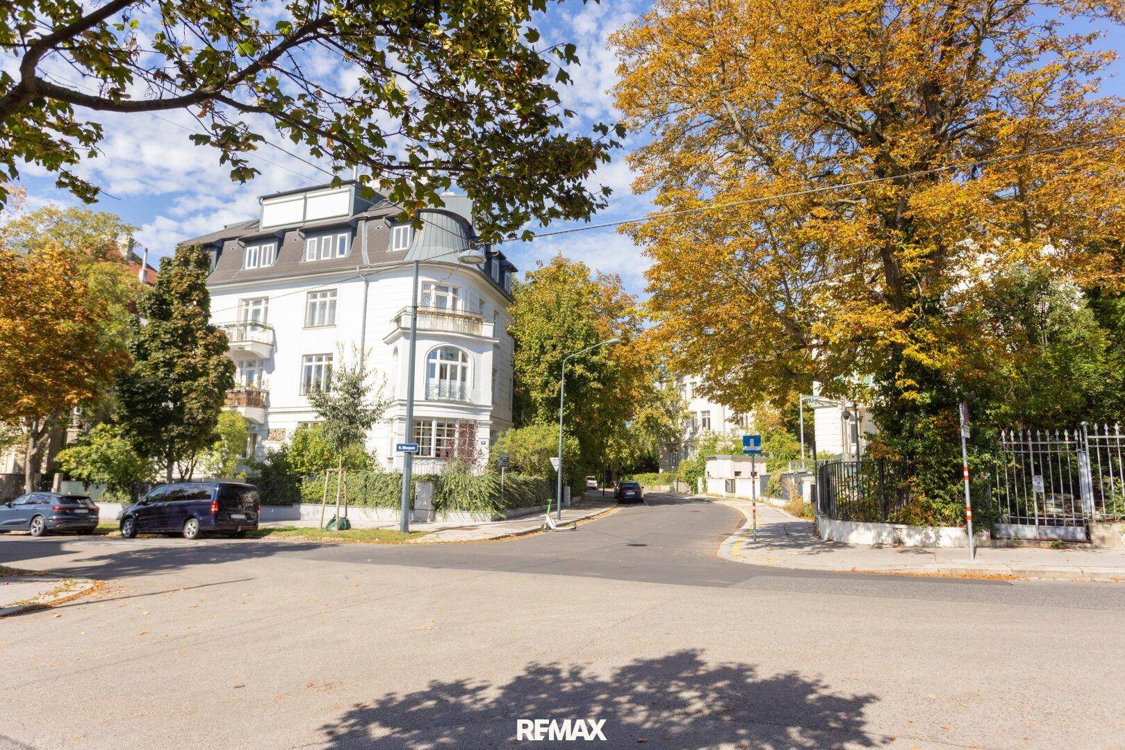 Historisches Gebäude an einer ruhigen Straße, umgeben von herbstlichen Bäumen.