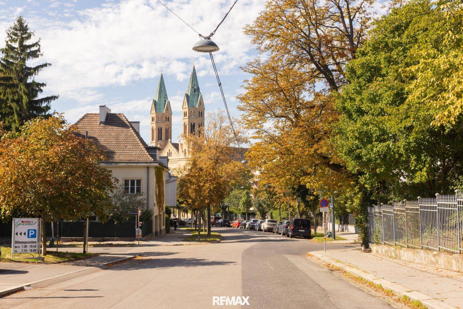 Ruhige Wohnstraße mit Blick auf eine Kirche und herbstliche Bäume.