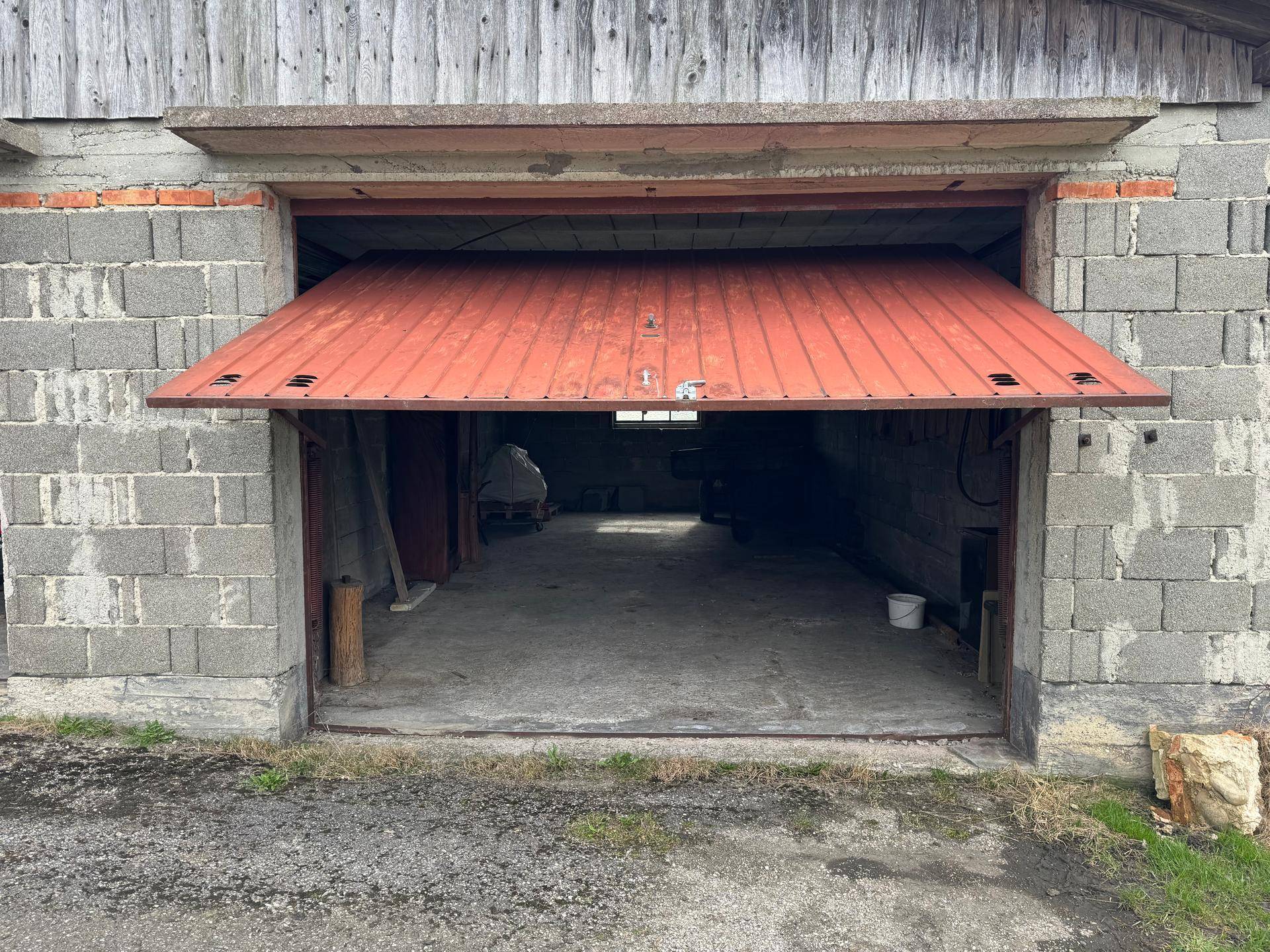 Außenansicht einer Garage mit teilweise geöffnetem roten Metalltor, die den Blick ins Innere freigibt.