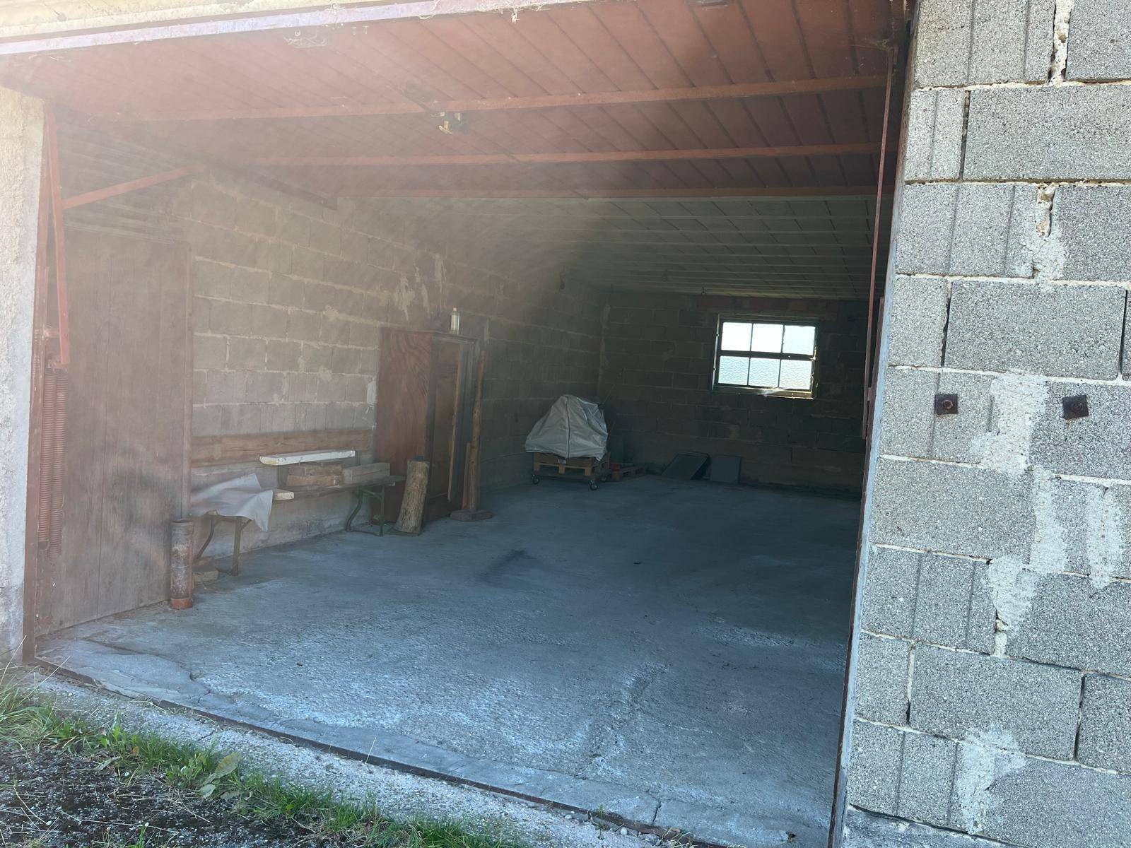 Innenansicht einer Garage mit robusten Betonsteinwänden und einem einfachen Betonboden, durch das offene Tor sichtbar.