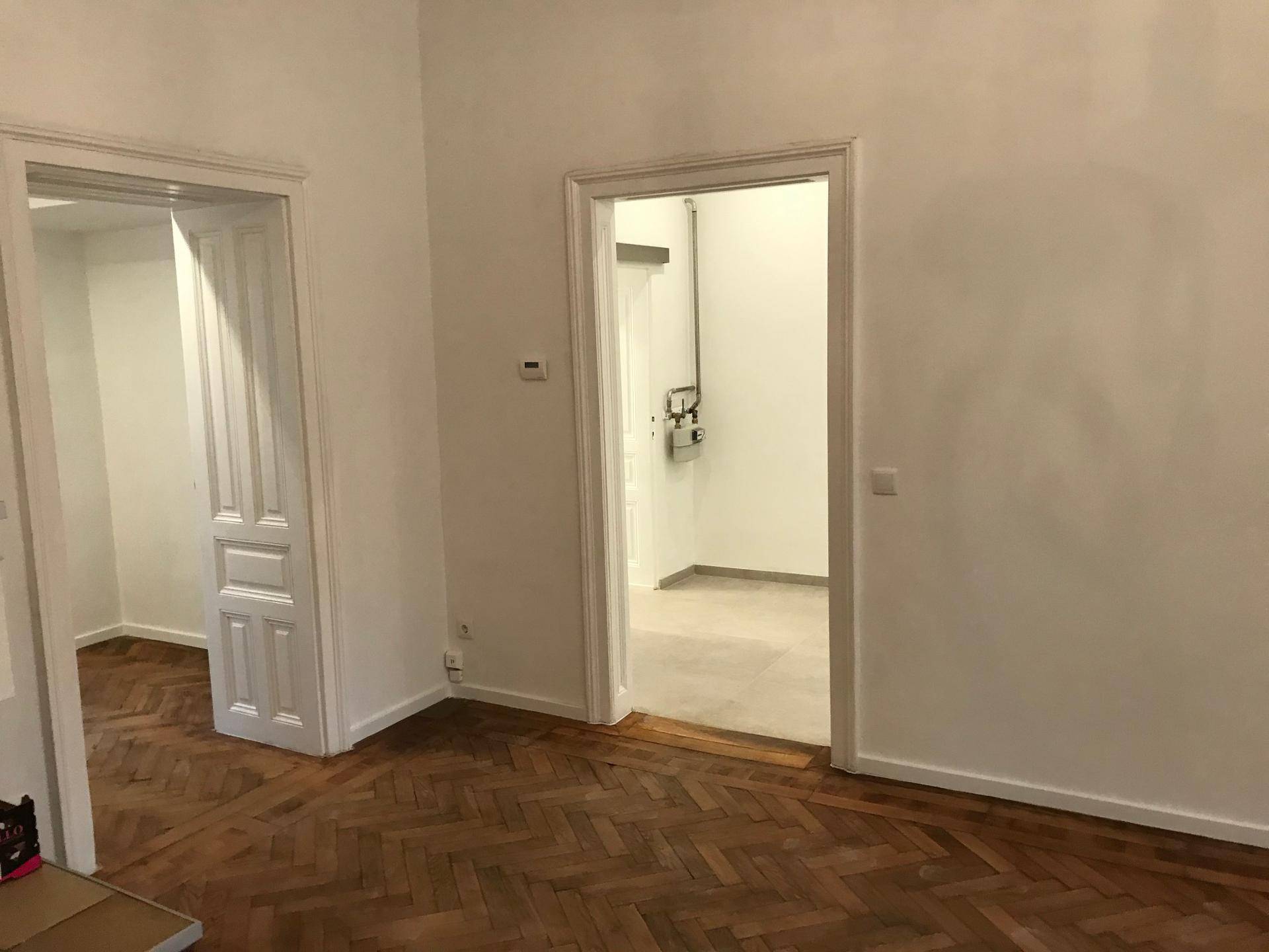 Geräumiges Zimmer mit klassischem Fischgrätparkett und zwei offenen Türrahmen, die zu weiteren Räumen führen.