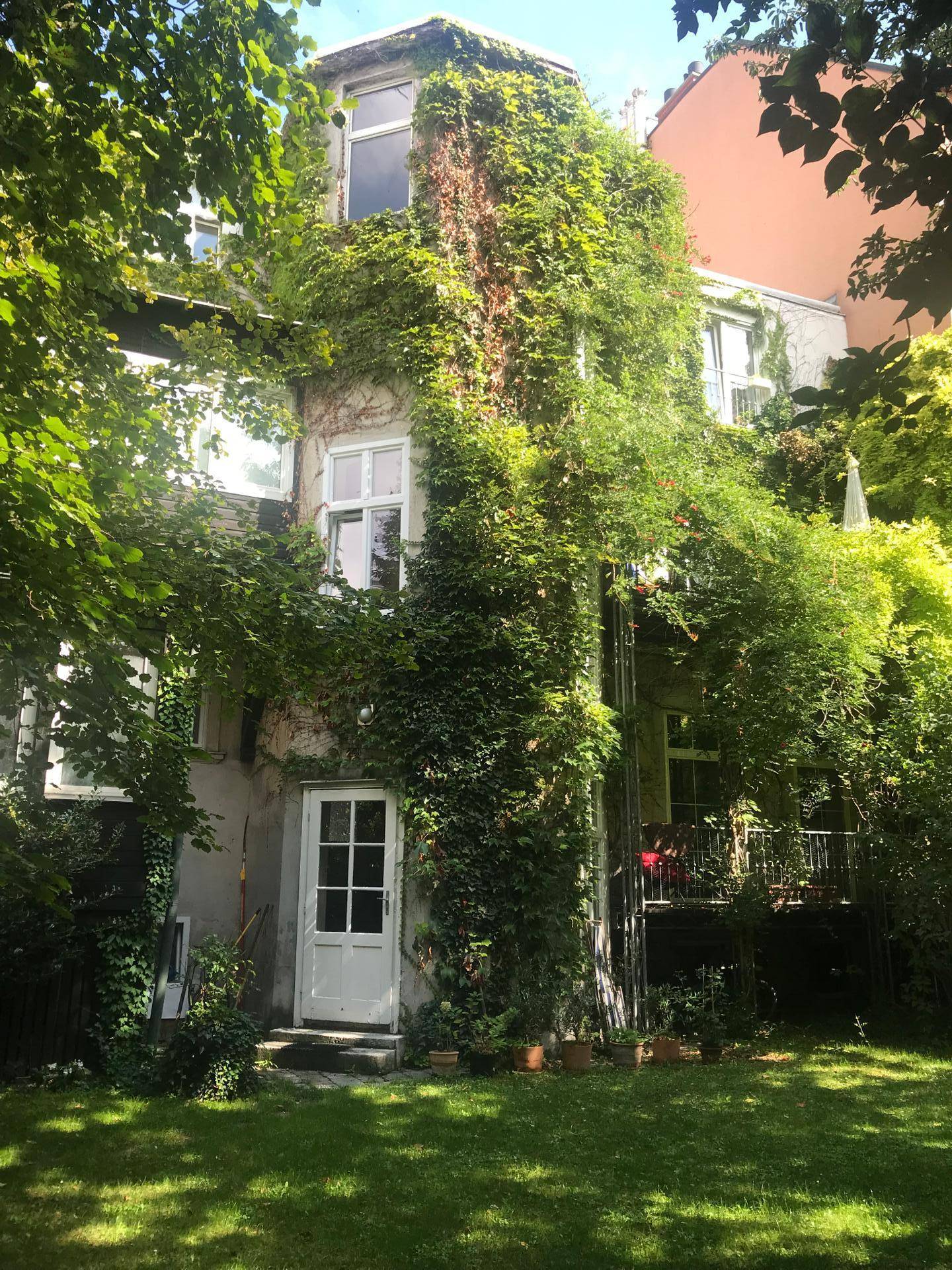 Malerischer Hinterhofgarten mit üppigem Grün, Efeu bewachsenem Haus und einem kleinen Balkon.