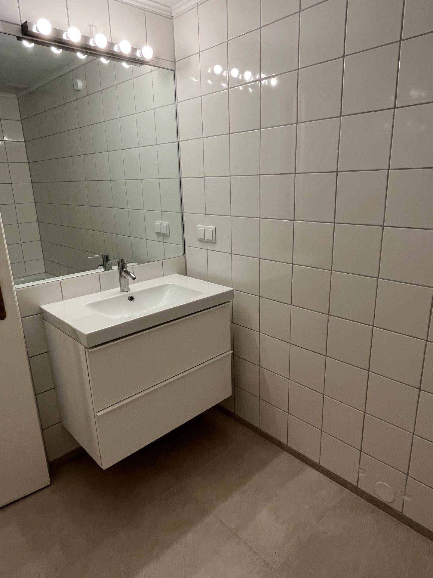 Modernes Badezimmer mit weißem Waschtischunterschrank, großem Spiegel und hellen quadratischen Wandfliesen.