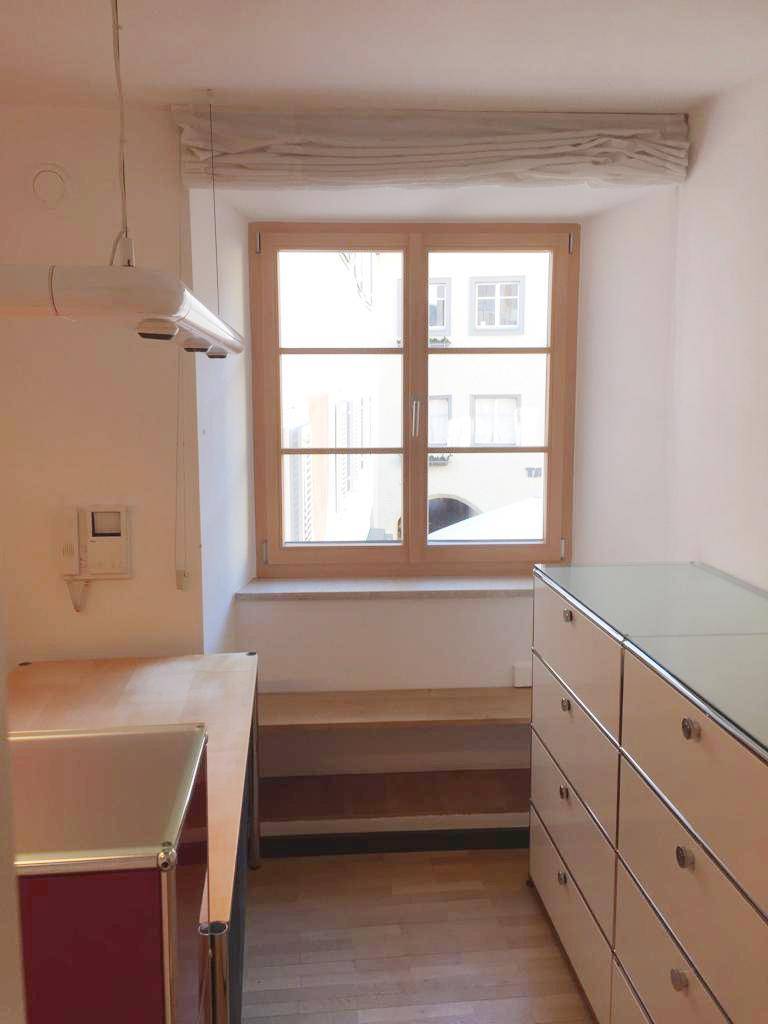 Heller Raum mit Holzfenster und Parkettboden, ausgestattet mit Schränken und einer Arbeitsfläche.