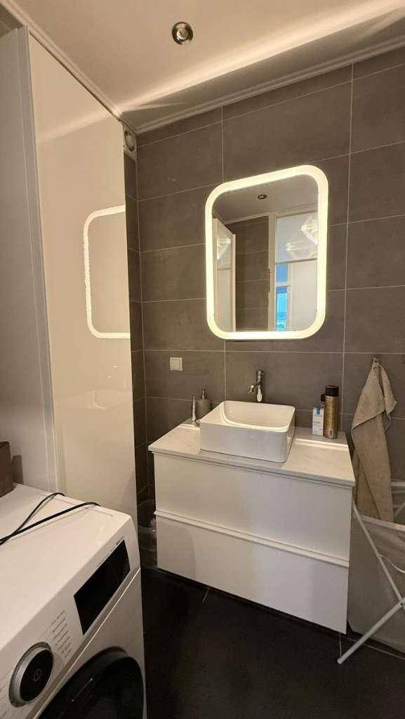 Modernes Badezimmer mit Waschbecken, beleuchtetem Spiegel und Waschmaschine.