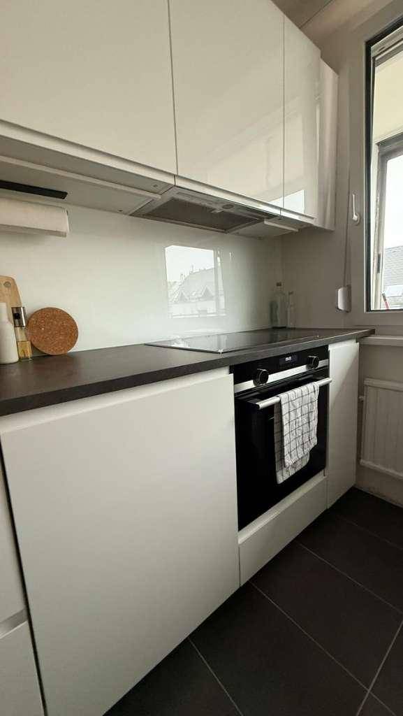 Moderne Küche mit weißen Hochglanzschränken, dunkler Arbeitsplatte und integriertem Backofen.
