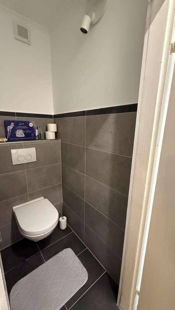 Separate Gästetoilette mit dunklen Fliesen und wandmontiertem WC.